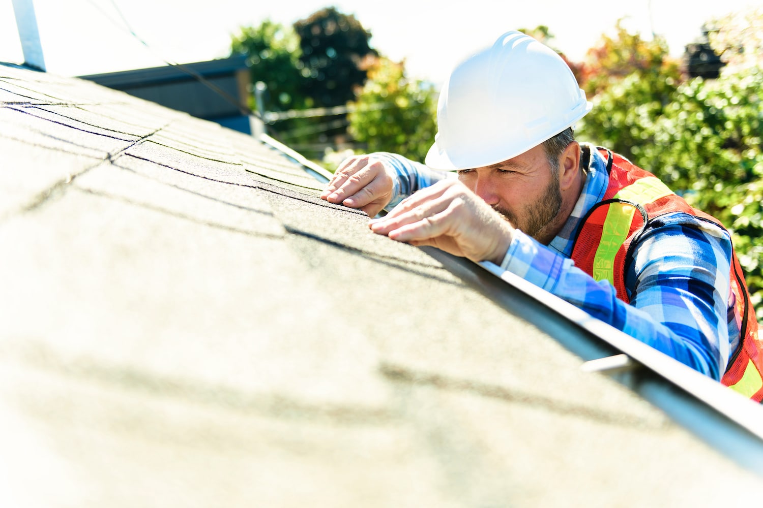 A man with hard hat standing on steps inspecting house roof