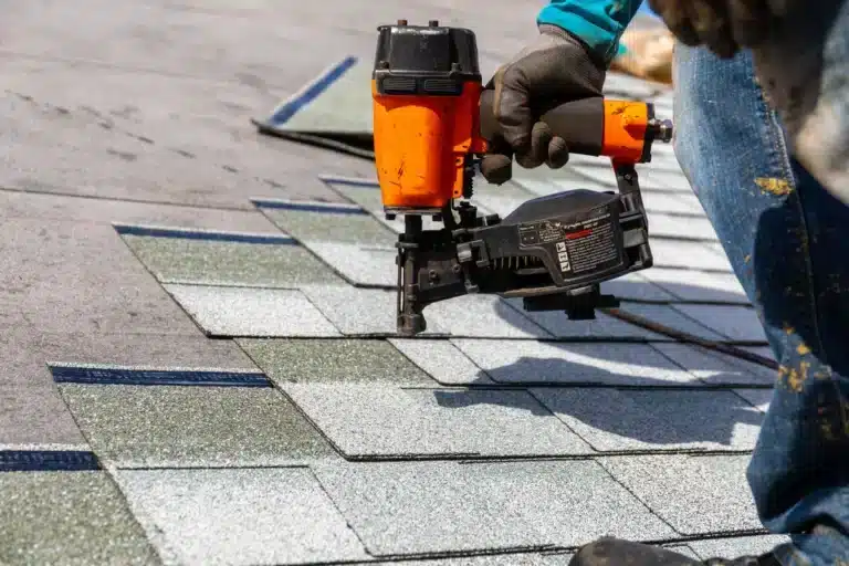 contractor using nail gun to nail shingles down onto roof