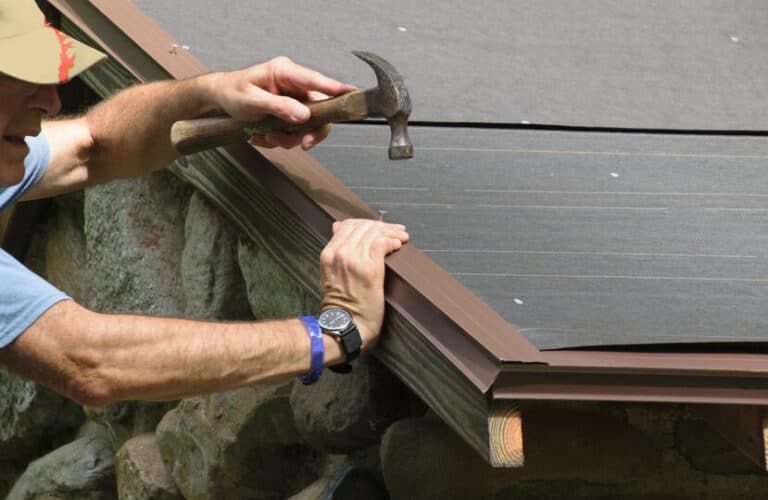 how to install drip edge-close up of a man using a hammer to nail drip edge materials to a roof