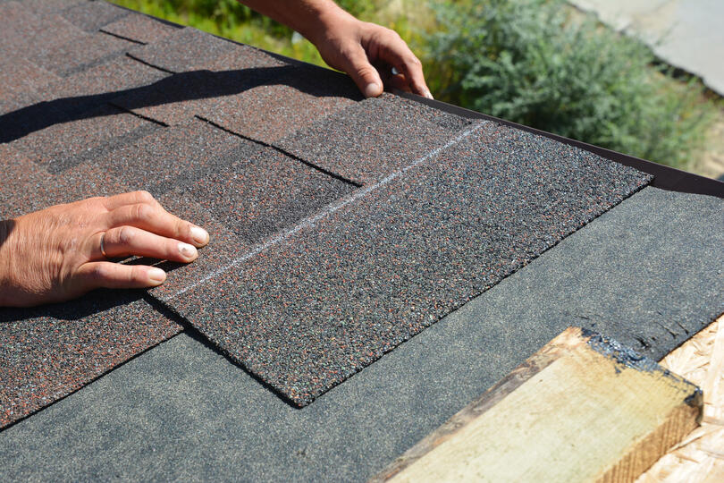 how to start shingles on a roof-close up of hands placing shingles to nail them to a roof